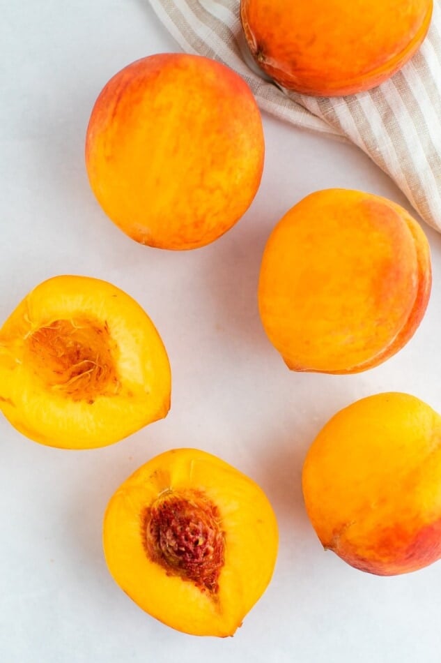 Fresh peaches on a marble surface. One is halved.