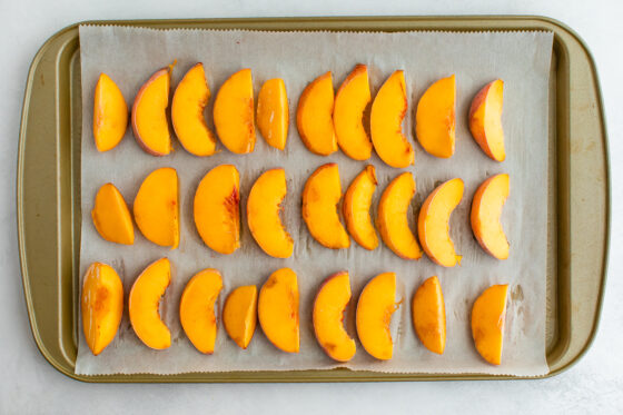 Fresh peaches in three rows on a parchment lined baking sheet, ready for freezing.