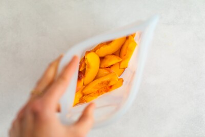 Frozen peaches in a clear Stasher bag. Woman's hand holding the bag open so you can see the frozen peaches.