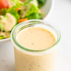 A jar of easy hummus dressing. A salad is out of focus in the background.