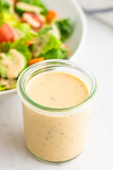 A jar of easy hummus dressing. A salad is out of focus in the background.