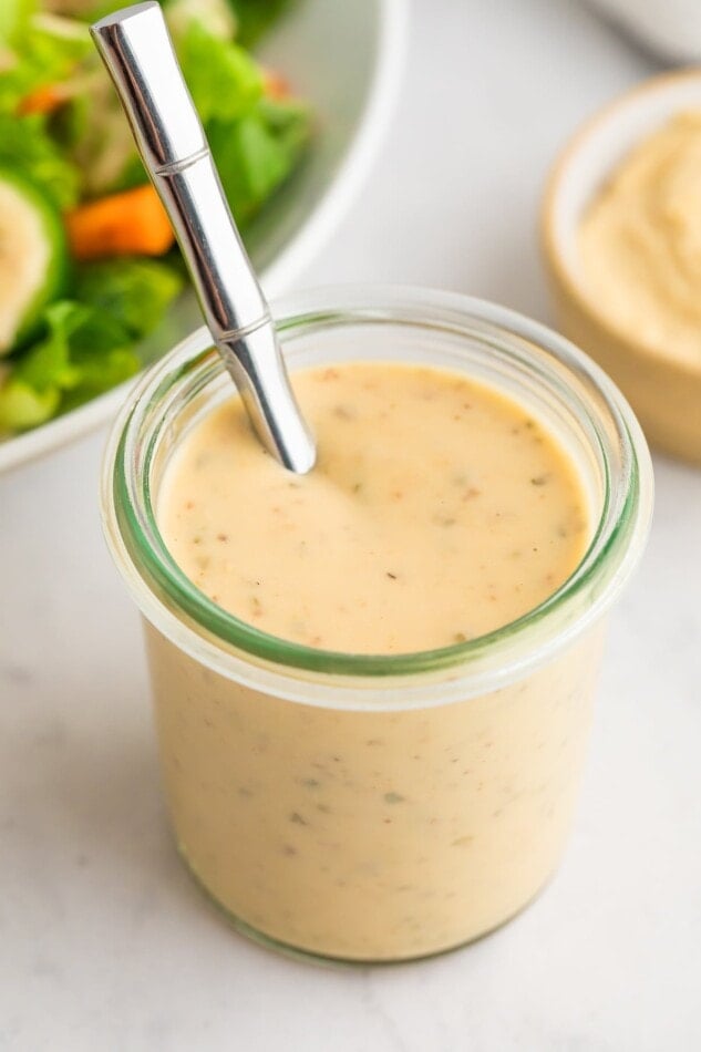 A jar of easy hummus dressing. A silver spoon is poking out of the top.