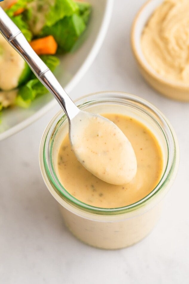 A jar of easy hummus dressing with a spoon ladling some dressing out.