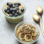 Two glass bowls of overnight steel cut oats. One it topped with blueberries and the other is topped with banana, maple and chia seeds.