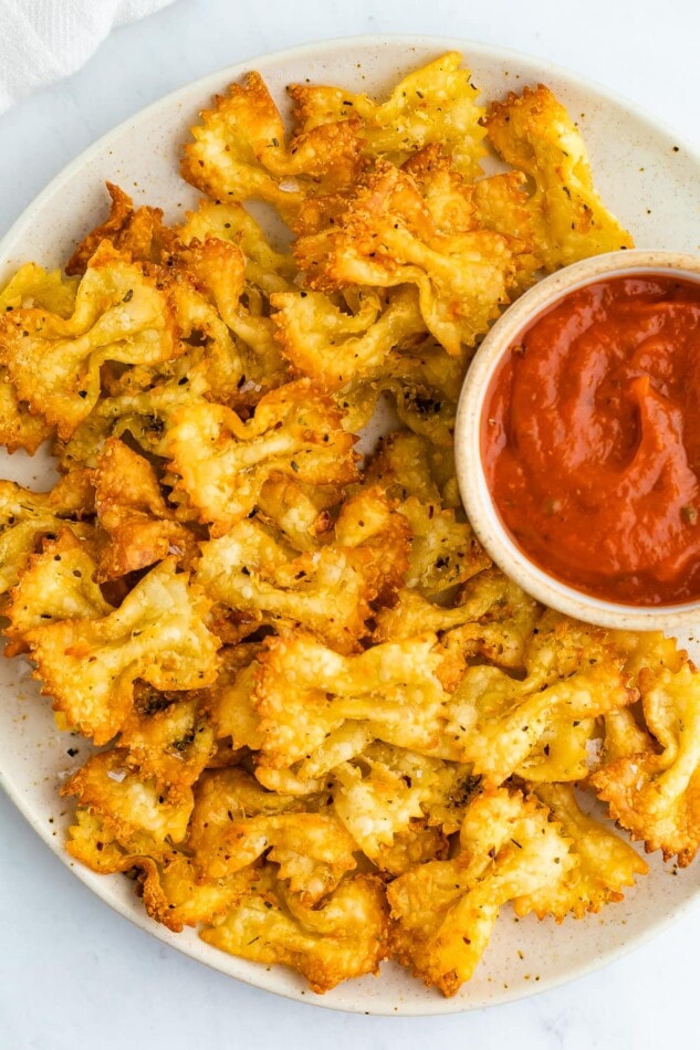 Pasta chips on a plate with a small bowl of marinara for dipping