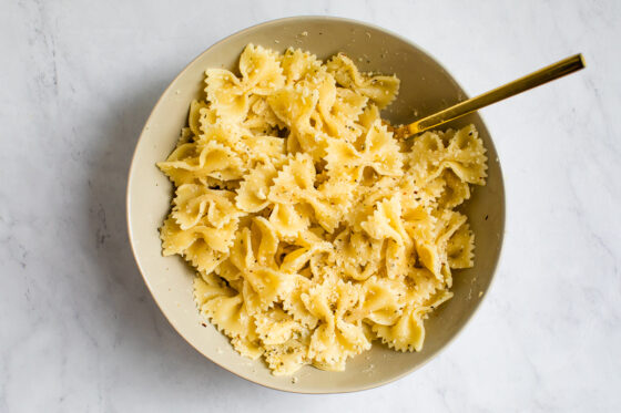 Cooked pasta being tossed in a bowl with a gold spoon.