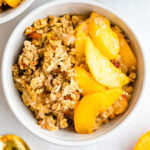 Up close shot of peach crisp in a bowl with a gold spoon on the side.