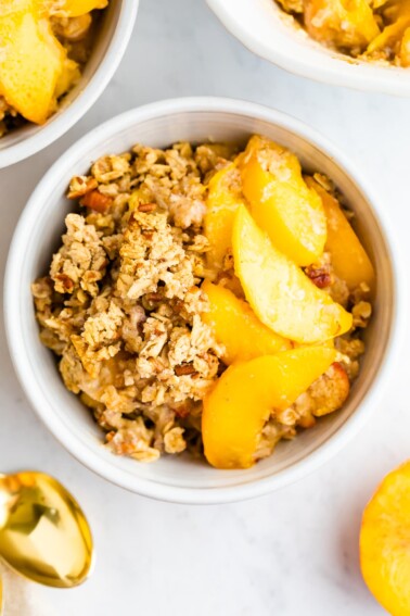 Up close shot of peach crisp in a bowl with a gold spoon on the side.