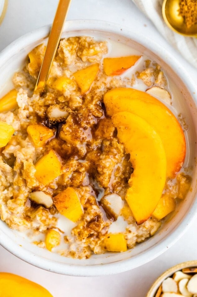 Peaches and cream oatmeal in a white bowl with fresh peaches and oat milk on top.