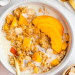 Peaches and cream oatmeal in a white bowl with fresh peaches and oat milk on top.