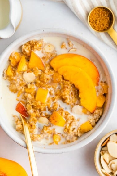 Peaches and cream oatmeal in a white bowl with fresh peaches and oat milk on top.