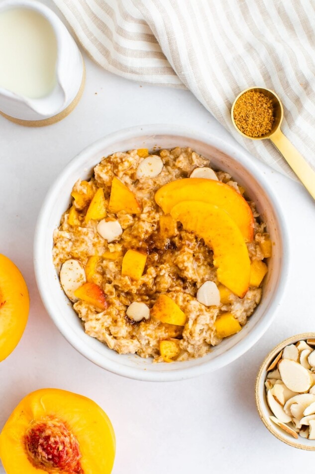 Peaches and cream oatmeal in a white bowl with fresh peaches and almonds on top.