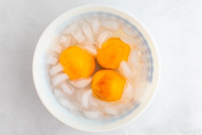 Three peaches in an ice water bath after blanching.