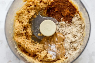 A food processor with blended chickpeas, nut butter, protein powder, coconut sugar and salt.
