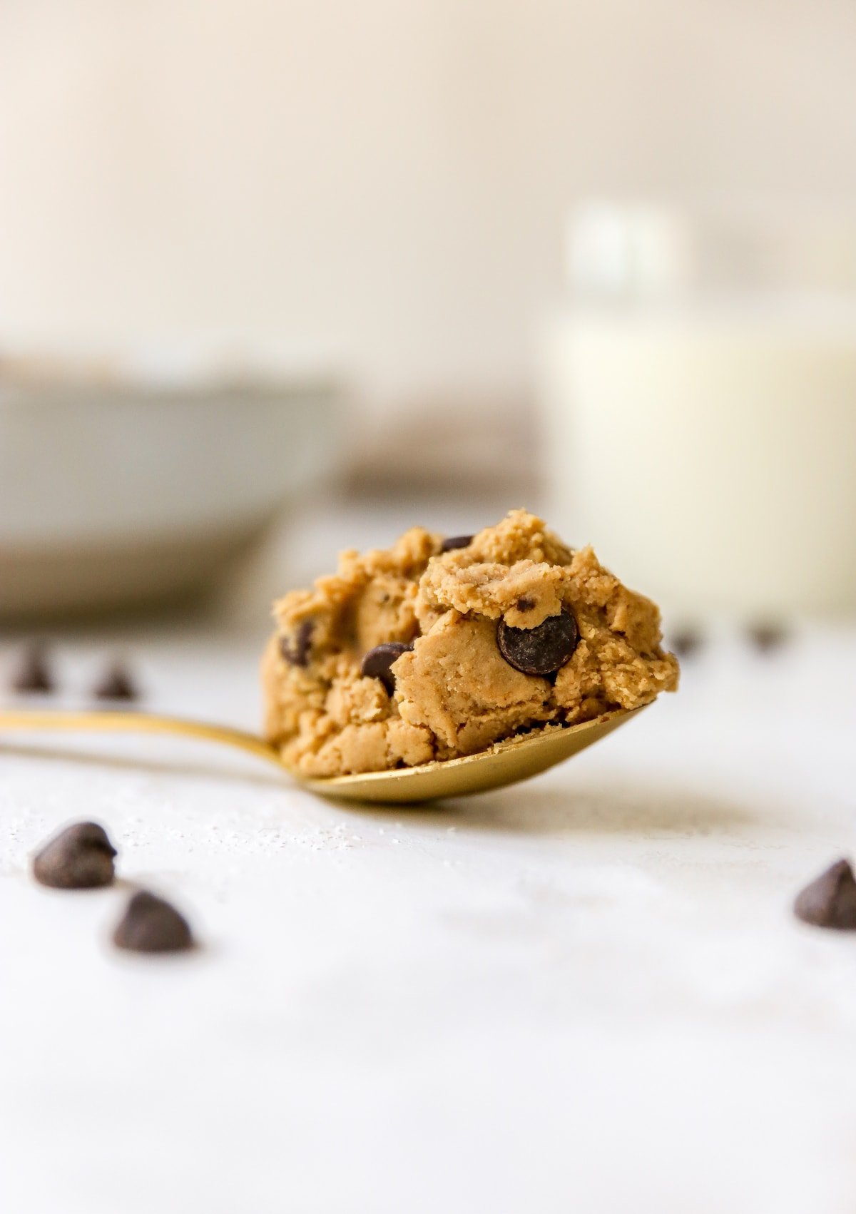 A gold spoon on a white surface with a scoop of protein cookie dough.