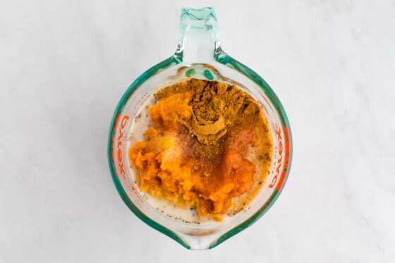Cinnamon, pumpkin, almond milk and chia seeds in a glass measuring cup.