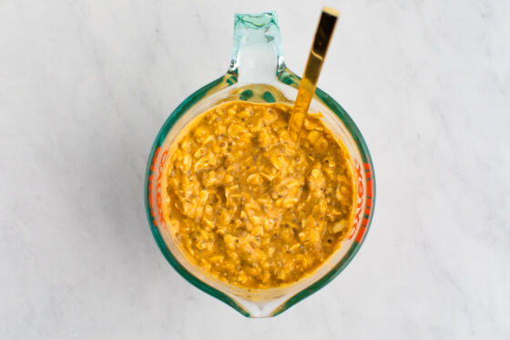 Glass measuring cup with a spoon mixing the pumpkin overnight oats mixture.