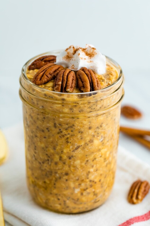 Jar of pumpkin pie overnight oats topped with pecans, whipped cream and cinnamon.