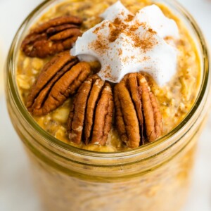 Jar of pumpkin pie overnight oats topped with pecans, whipped cream and cinnamon.