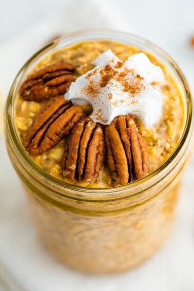 Jar of pumpkin pie overnight oats topped with pecans, whipped cream and cinnamon.
