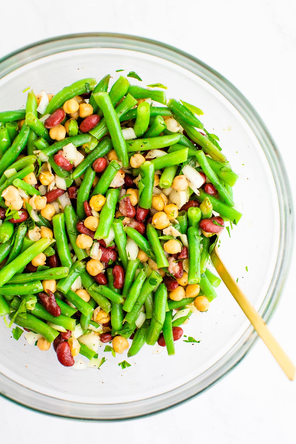 Mixing bowl with a spoon and three bean salad, a salad made with chickpeas, kidney beans, onion and green beans.