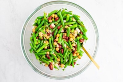 Mixing bowl with a spoon and three bean salad, a salad made with chickpeas, kidney beans, onion and green beans.