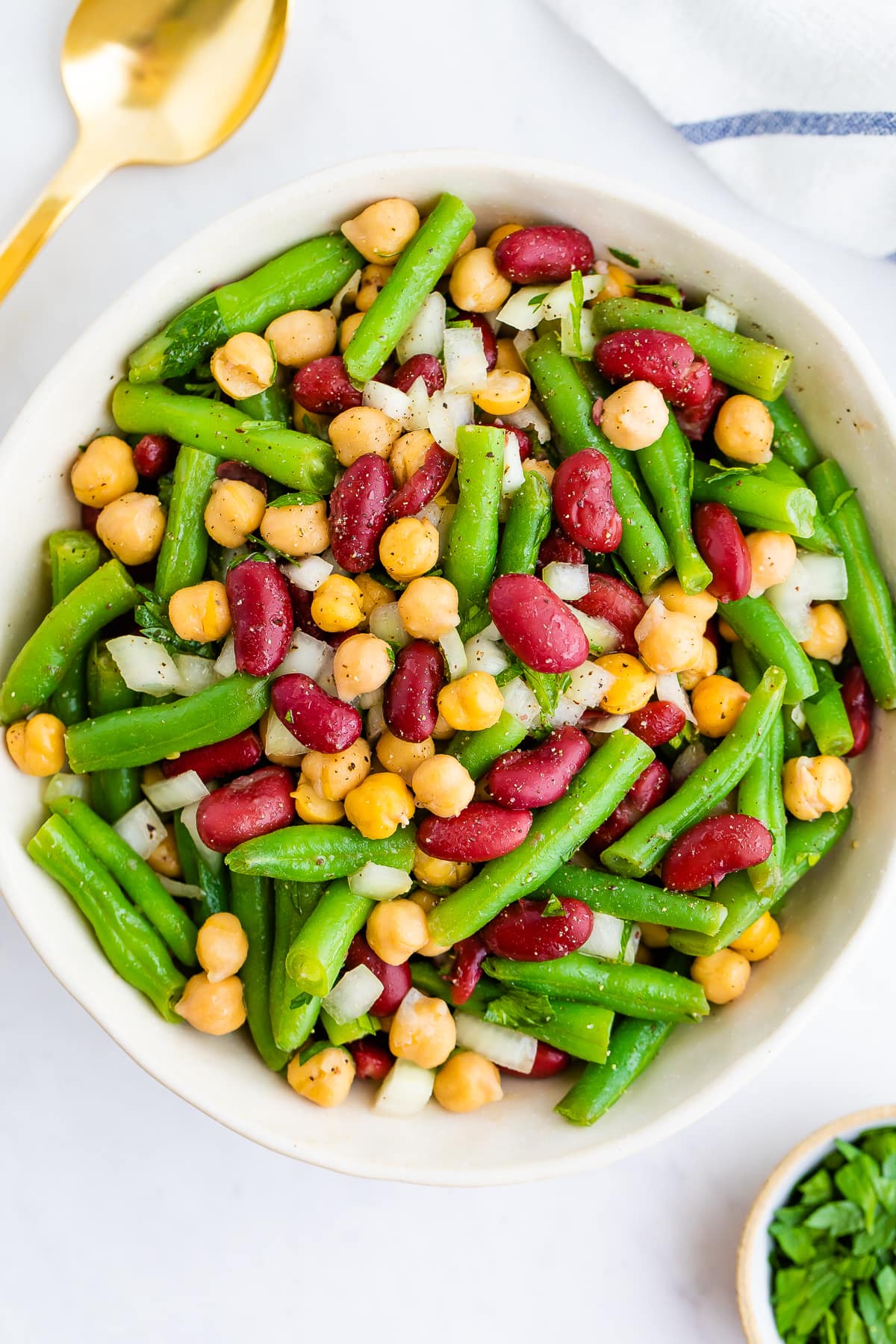 Serving bowl with three bean salad, a salad made with chickpeas, kidney beans, onion and green beans.