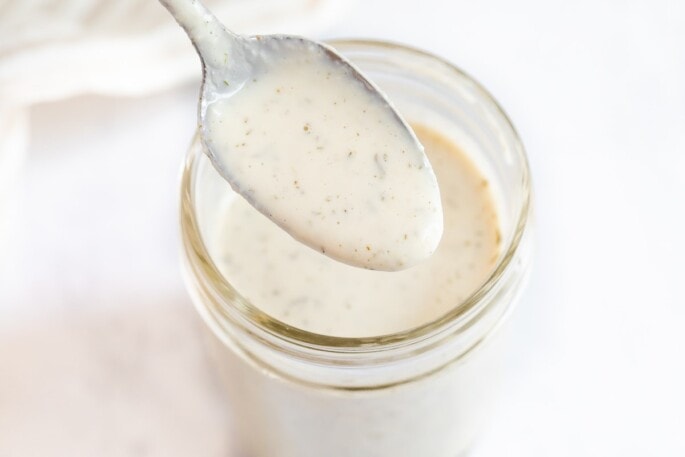 Spoon with vegan ranch dressing from a mason jar.