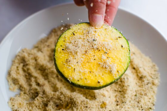 Person dipping a zucchini slice in seasoned almond flour.