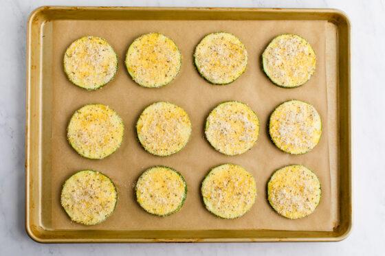 Zucchini slices covered in seasoned almond flour breading on a cookie sheet.