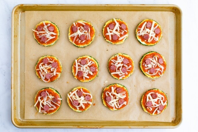 Unbaked zucchini pizza bites on a cookie tray.