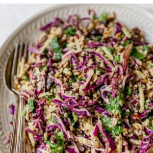 Plate with serving utensils with an apple slaw made with cabbage and quinoa.