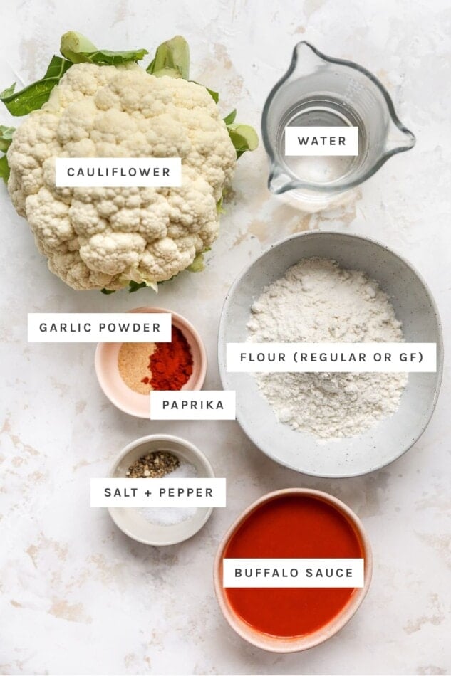 Ingredients measured out to make buffalo cauliflower wings: cauliflower, water, garlic powder, paprika, flour, buffalo sauce, salt and pepper.