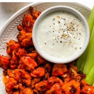 Plate of buffalo cauliflower wings served with vegan cashew ranch and celery sticks.