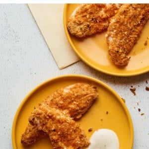 Overhead shot of baked chicken tenders on 2 plates with dipping sauce.