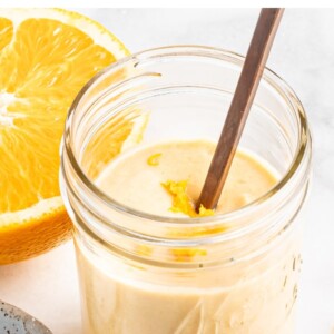 Jar of citrus tahini dressing with a spoon and topped with orange zest.