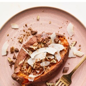 An overhead shot of a dessert sweet potato with topping sprinkled around. A gold fork rests on the plate next to the potato.