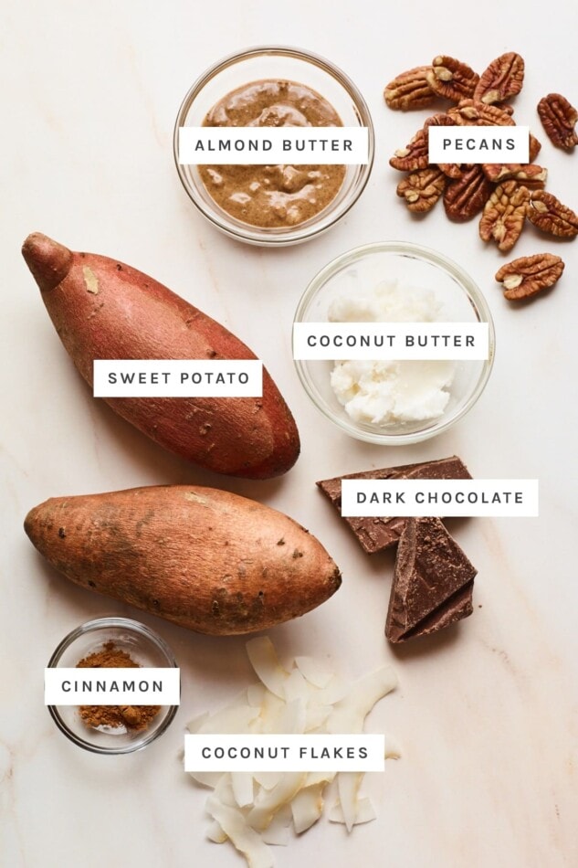 Ingredients measured out to make dessert baked sweet potatoes: almond butter, pecans, coconut butter, sweet potatoes, dark chocolate, cinnamon and coconut flakes.