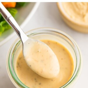 Spoon with a spoonful of hummus dressing from a jar.