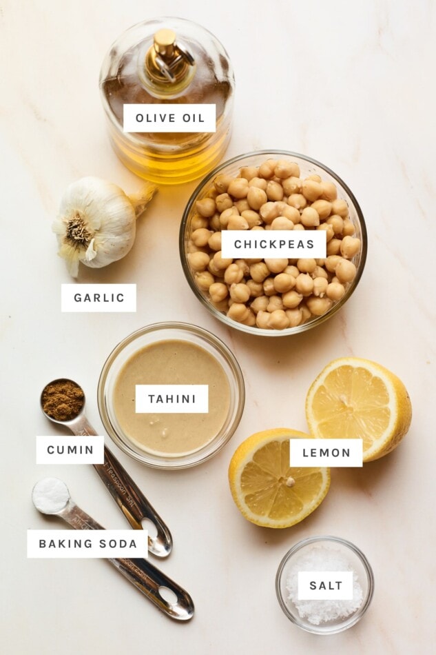 Ingredients measured out to make hummus: olive oil, chickpeas, garlic, tahini, lemon, cumin, baking soda and salt.