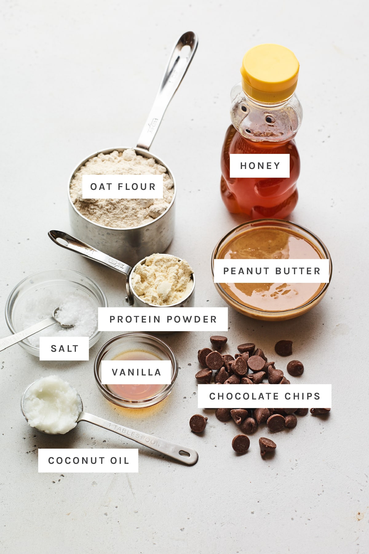 Ingredients measured out to make protein bars: honey, oat flour, protein powder, peanut butter, salt, vanilla, chocolate chips and coconut oil.