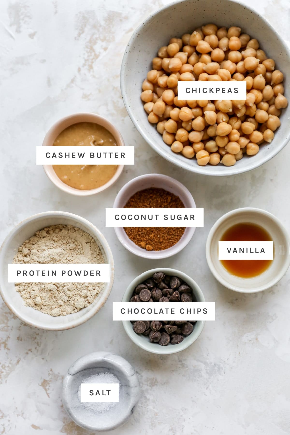 Ingredients measured out to make protein cookie dough: chickpeas, cashew butter, coconut sugar, vanilla, protein powder, chocolate chips and salt.
