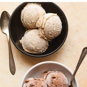 Two bowls of protein ice cream. One has chocolate ice cream and one has vanilla. Spoons are in or beside the bowls.