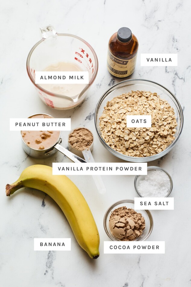 Ingredients measured out to make no bake protein cookies: almond milk, vanilla, oats, peanut butter, protein powder, oats, banana, salt and cocoa powder.