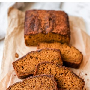 Loaf of pumpkin bread on a parchment paper resting on a cutting board. 4 slices have been cut from the loaf.