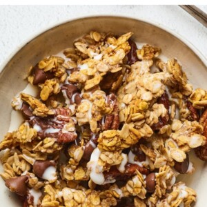 A bowl of pumpkin granola served in a bowl with milk. A silver spoon rests aside the bowl.