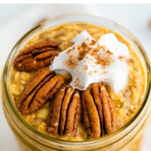 Jar of pumpkin pie overnight oats topped with pecans, whipped cream and cinnamon.