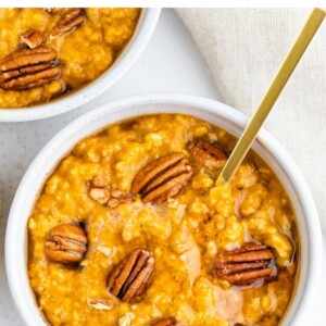 Bowl of pumpkin oatmeal topped with pecans and maple syrup.