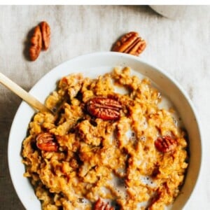 Bowl of pumpkin pie oatmeal topped with almond milk and pecans.