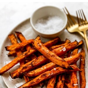 A plate of air fryer sweet potato fries with two forks and a ramekin of salt.